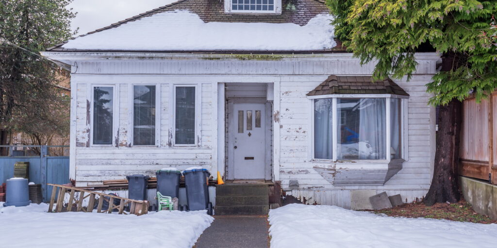 white run down bungalow with overflowing garbage cans in front