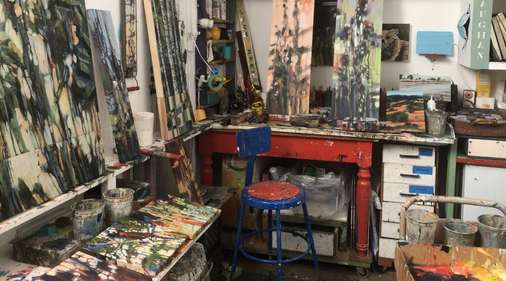 artist's studio with abstract apintings, paint palettes, masking tape, desk and chair