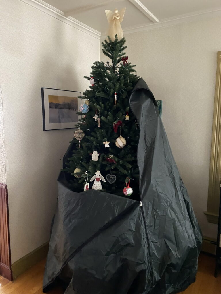 fake decorated Christmas tree with angel on top halfway covered by a tree bag