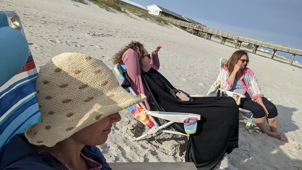 editors Cheryl Wilder, Suzanne Farrell Smith, and Claire Guyton sit in beach chairs on a cold sunny day on a sandy beach