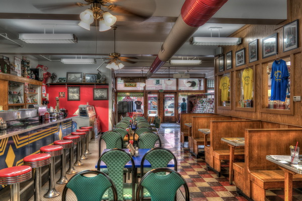 50s diner with green chairs, blue tables, red barstools, and miscellaneous brick-brack on the walls and shelves