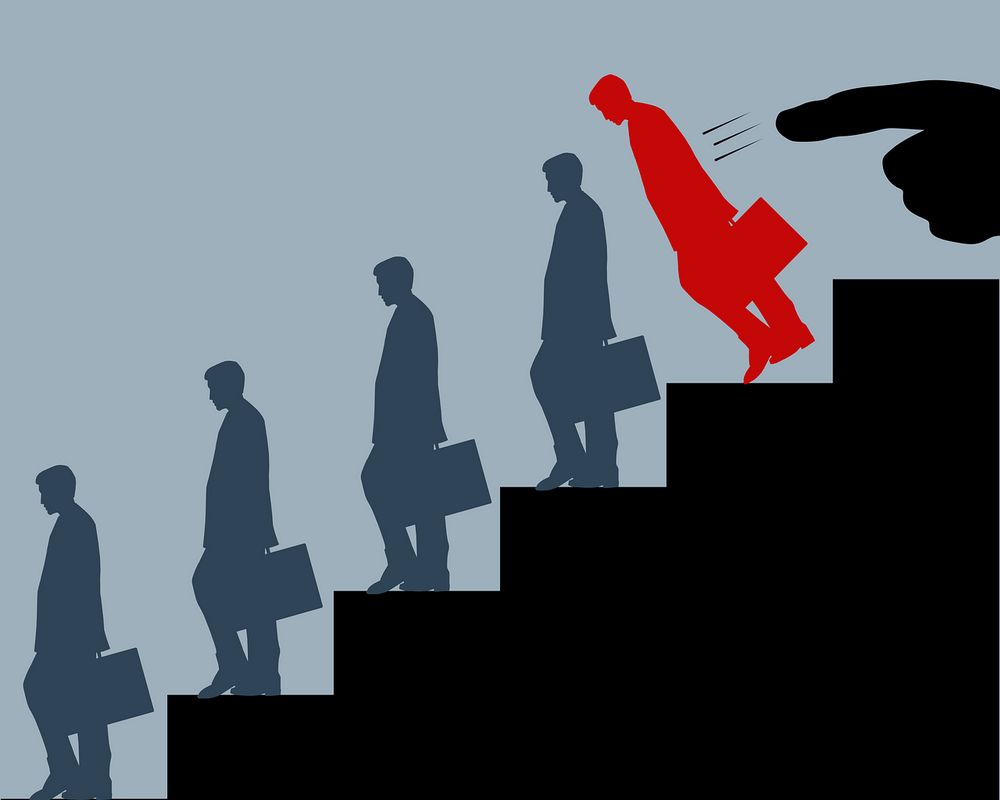 Graphic illustration of a black staircase with the same blue silhouette of a business person on each step and the person on top is a red silhouette being pushed down by a large pointer finger