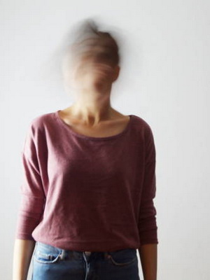 Portrait of confused young woman with blurred face. She is moving her head fast, so her face isn't identifiable. 