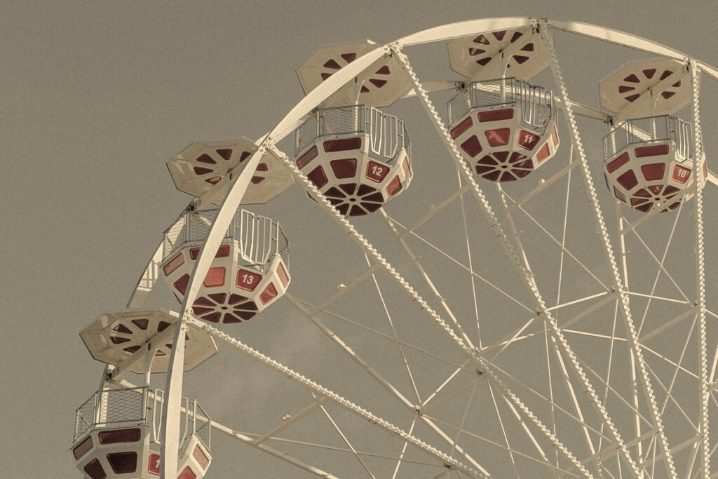 empty red and white gondola cabins on a white Ferris wheel against a grainy blue-grey sky